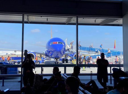 Photo from inside an airport terminal showing silhouettes of people looking out at passengers deplaning from a Southwest jet on the tarmac.