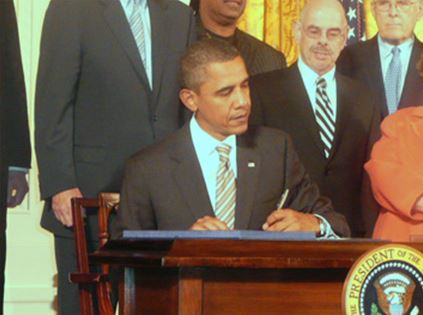 President Obama signing CVAA into law and surrounded by others.